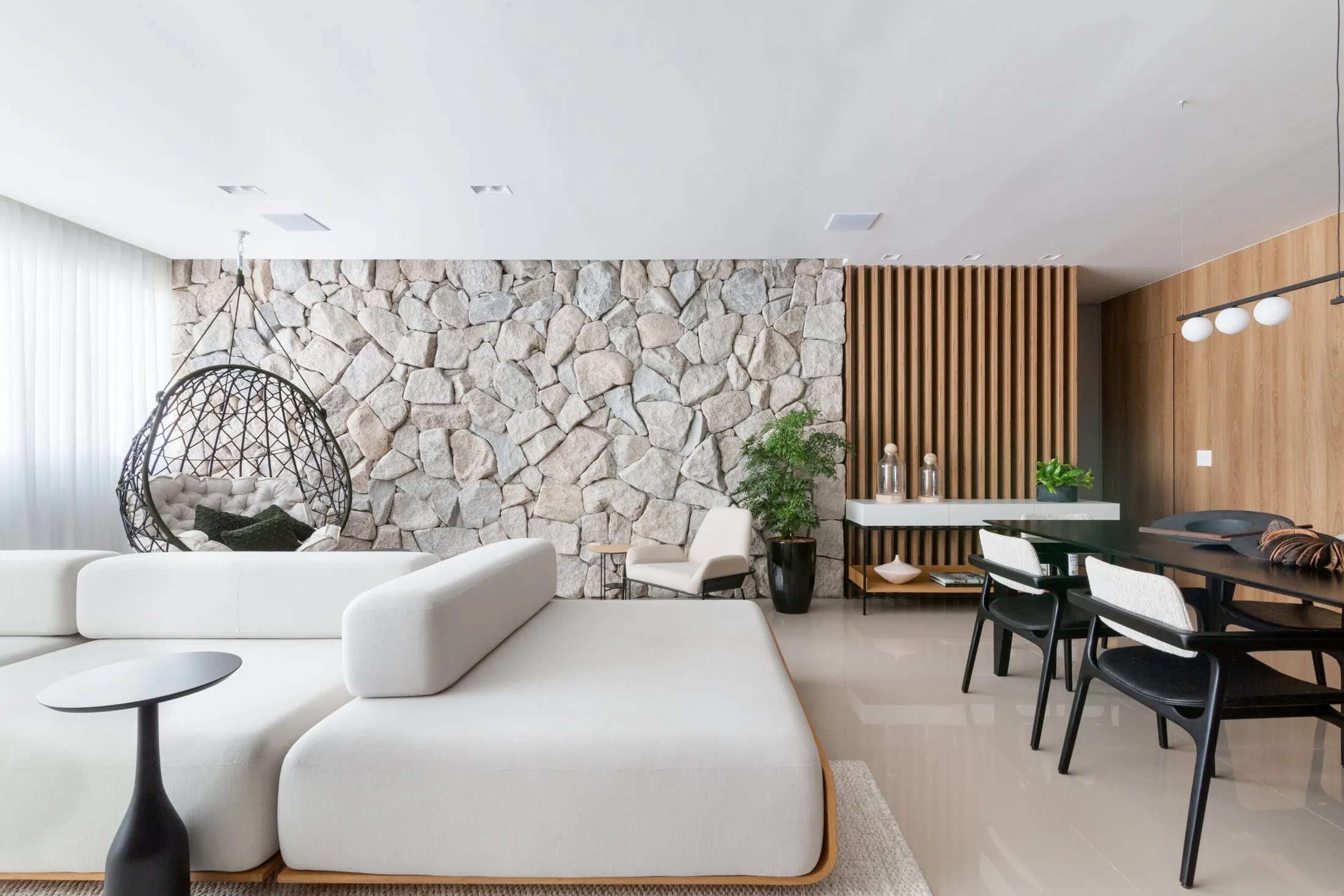 Sala de estar integrada com parede de pedra, painel ripado de madeira e sofá claro