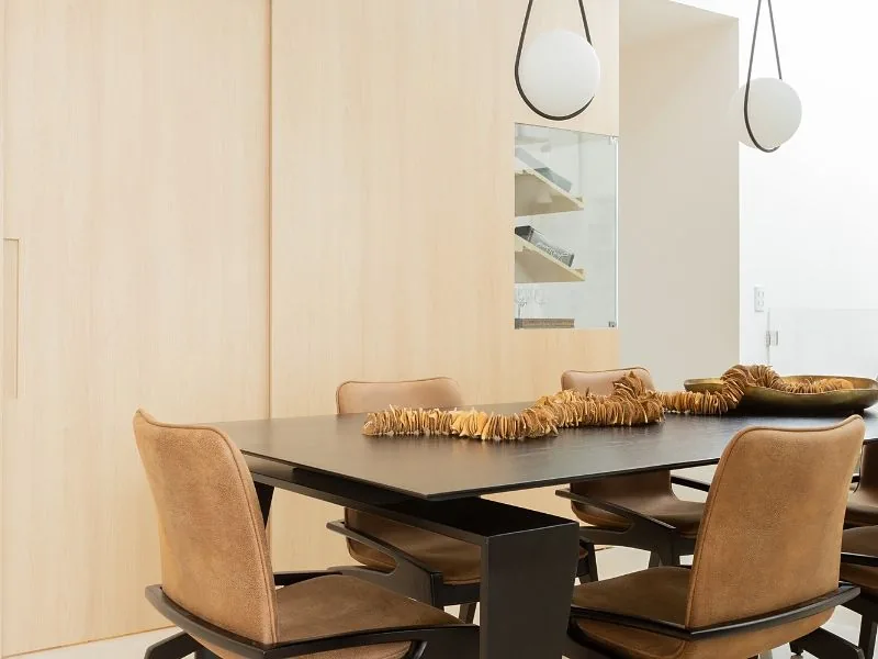 Sala de jantar com painel de madeira clara, mesa preta e cadeiras de couro caramelo
